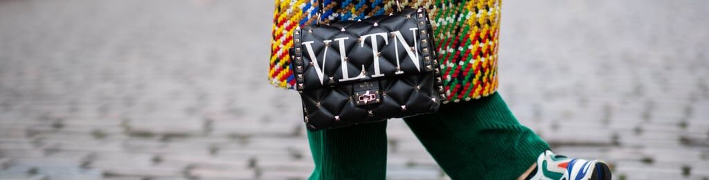 Close-up of a luxury Valentino (VLTN) crossbody bag worn with a colorful textured outfit and green socks, styled in a street fashion look.